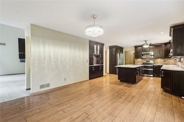 kitchen with sink, pendant lighting, decorative backsplash, a kitchen island, and appliances with stainless steel finishes