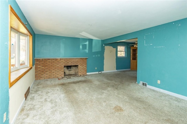 unfurnished living room with light carpet, a brick fireplace, and a wealth of natural light