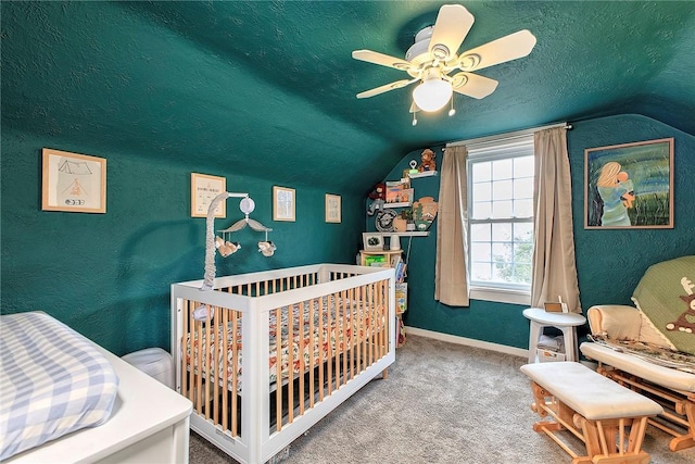 carpeted bedroom with a textured ceiling, vaulted ceiling, a nursery area, and ceiling fan