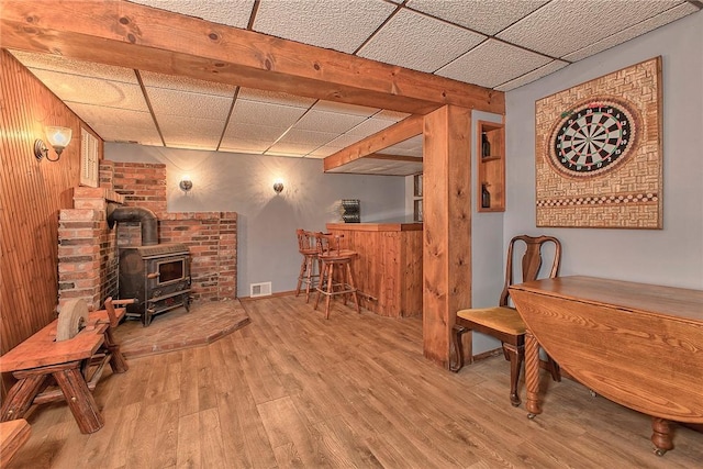 interior space with light wood-type flooring, a wood stove, a drop ceiling, and wooden walls