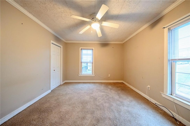 carpeted empty room featuring ceiling fan, a wealth of natural light, and crown molding