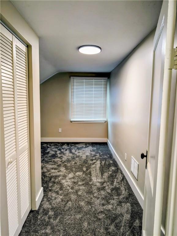 corridor with dark colored carpet, plenty of natural light, and lofted ceiling