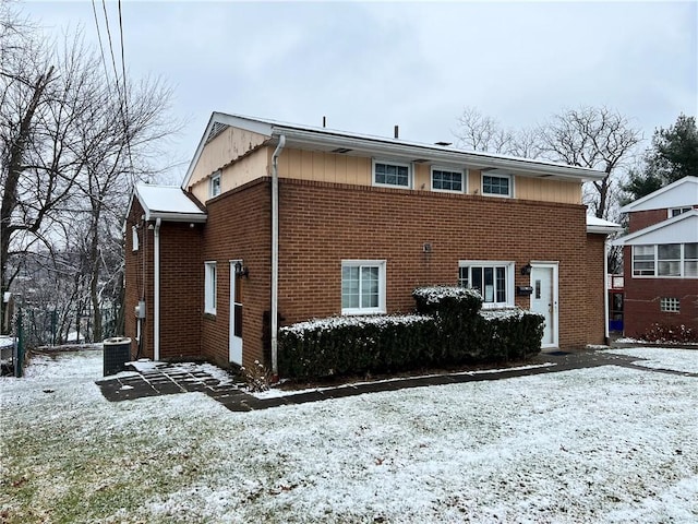 snow covered rear of property featuring central AC unit