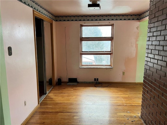 spare room with light hardwood / wood-style flooring and brick wall