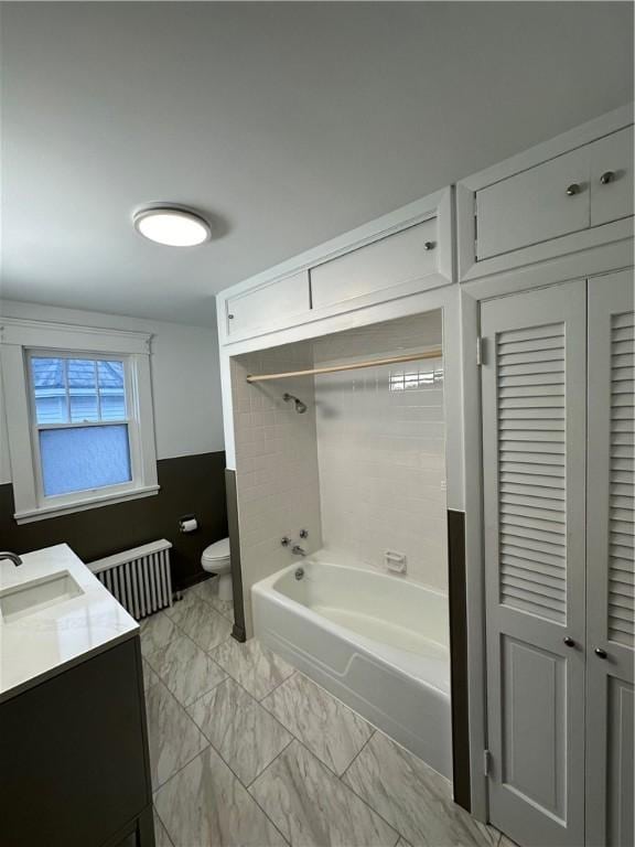 full bathroom with tiled shower / bath, radiator, vanity, and toilet