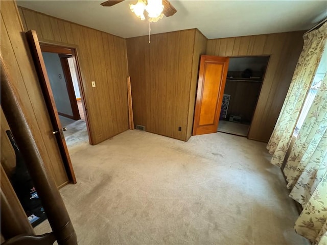 unfurnished bedroom with ceiling fan, a closet, light colored carpet, and wood walls