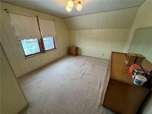 additional living space featuring lofted ceiling, light carpet, wooden walls, and an inviting chandelier