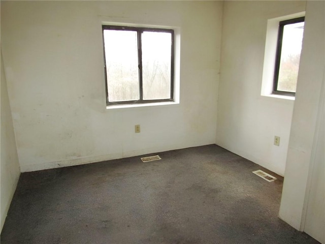 unfurnished room featuring a wealth of natural light and dark carpet