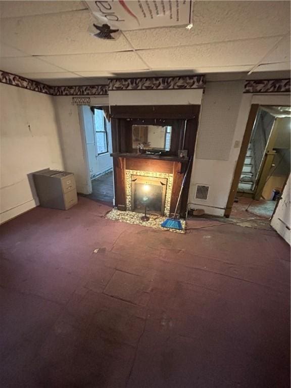 unfurnished living room with a paneled ceiling and a tiled fireplace