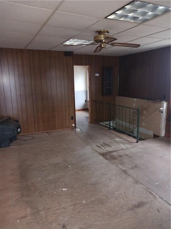 empty room featuring a paneled ceiling, ceiling fan, and wood walls