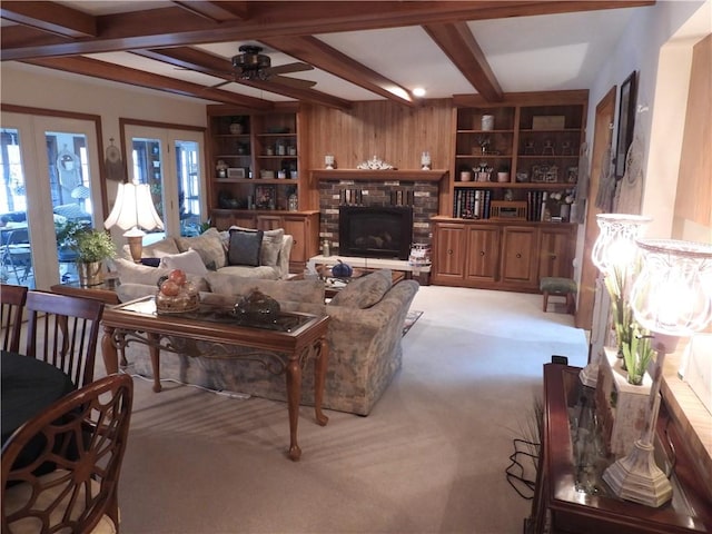 living room featuring ceiling fan, built in features, wood walls, light carpet, and a fireplace