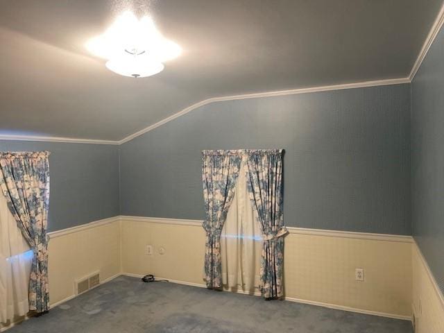 carpeted empty room featuring vaulted ceiling, wainscoting, visible vents, and crown molding