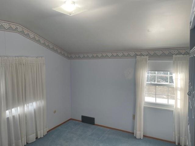 carpeted spare room featuring baseboards and vaulted ceiling