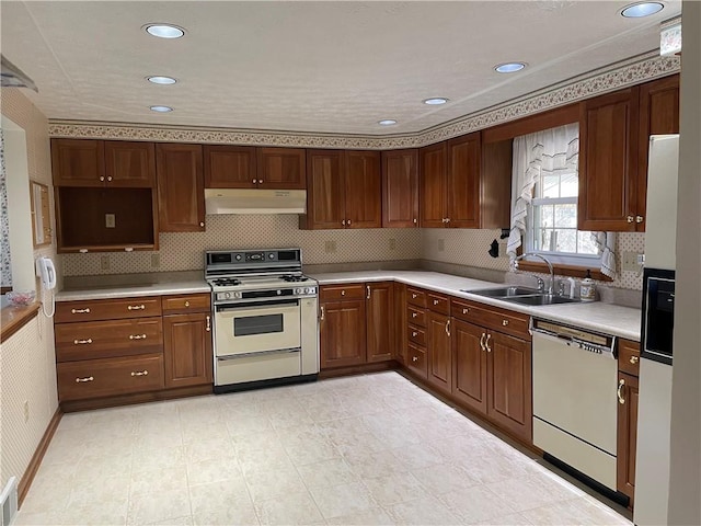 kitchen with a sink, decorative backsplash, white appliances, light countertops, and under cabinet range hood
