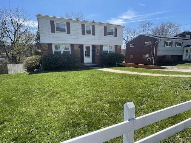 colonial-style house with fence, a front lawn, and brick siding