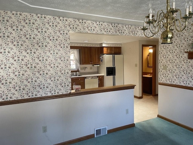 kitchen featuring wallpapered walls, an inviting chandelier, dishwasher, visible vents, and white fridge with ice dispenser