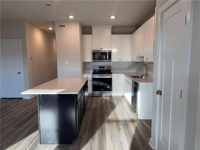 kitchen with white cabinets, hardwood / wood-style flooring, a kitchen island, and appliances with stainless steel finishes