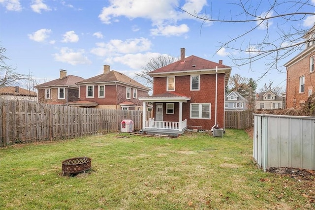 back of house with a lawn, a fire pit, central AC, covered porch, and a shed