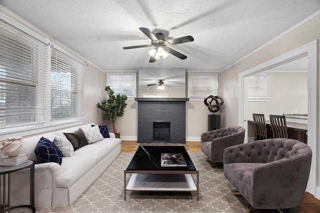 living room with a brick fireplace, ceiling fan, wood-type flooring, and ornamental molding