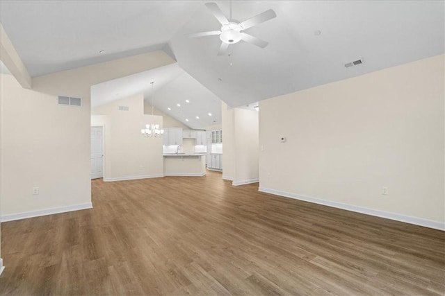 unfurnished living room featuring hardwood / wood-style flooring, ceiling fan with notable chandelier, and vaulted ceiling