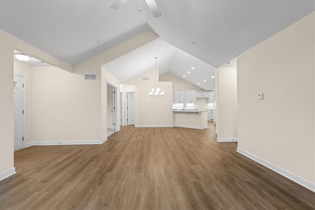 unfurnished living room with hardwood / wood-style floors, ceiling fan with notable chandelier, sink, and vaulted ceiling