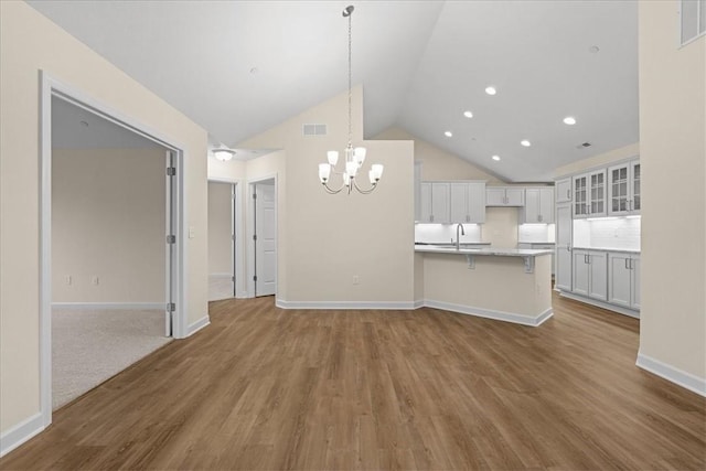 unfurnished living room featuring hardwood / wood-style floors, a notable chandelier, sink, and high vaulted ceiling