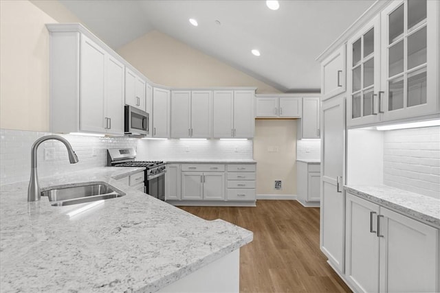 kitchen with sink, stainless steel appliances, tasteful backsplash, vaulted ceiling, and white cabinets