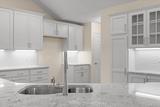 kitchen with tasteful backsplash, white cabinetry, sink, and light stone counters