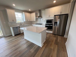 kitchen with white cabinets, wall chimney exhaust hood, appliances with stainless steel finishes, tasteful backsplash, and a kitchen island