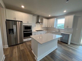 kitchen with appliances with stainless steel finishes, a kitchen island, sink, wall chimney range hood, and white cabinetry