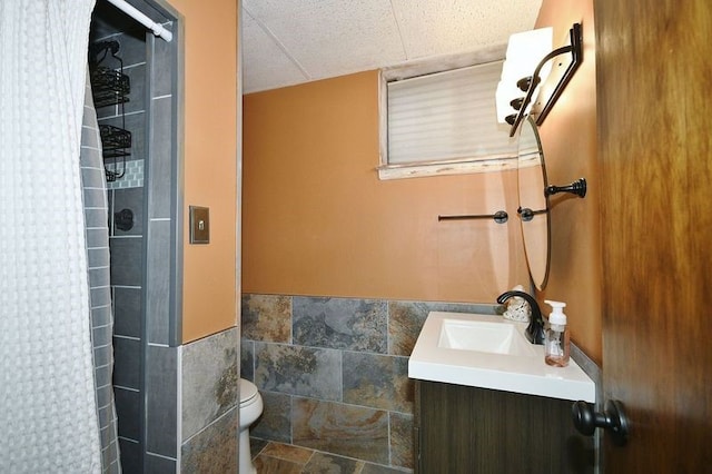 bathroom featuring vanity, toilet, tiled shower, and tile walls