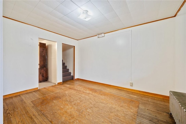 empty room featuring wood-type flooring, crown molding, and radiator