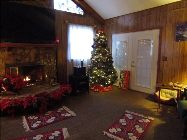 living room featuring carpet flooring, a stone fireplace, wooden walls, and vaulted ceiling