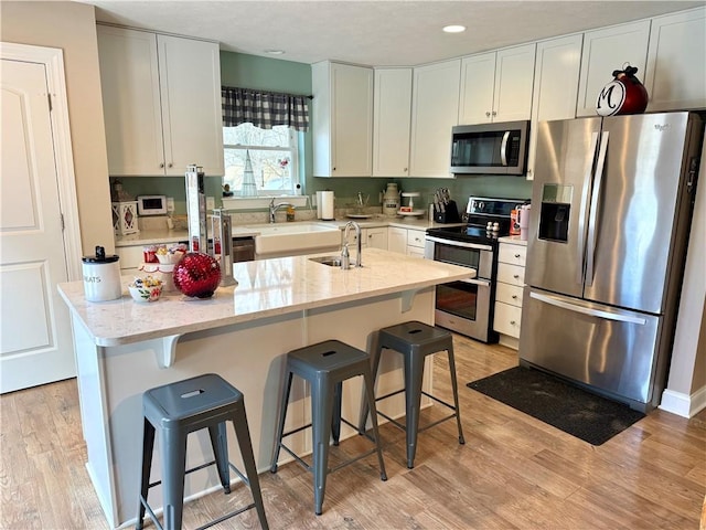 kitchen featuring white cabinets, appliances with stainless steel finishes, light hardwood / wood-style floors, and an island with sink