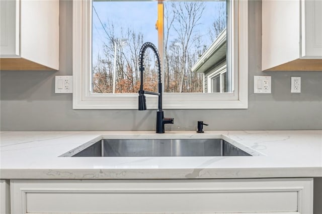 interior details with light stone counters, white cabinetry, and sink