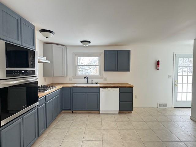 kitchen with sink, light tile patterned flooring, exhaust hood, and appliances with stainless steel finishes