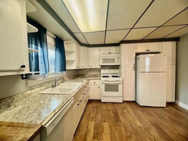 kitchen with light wood-type flooring, a drop ceiling, white appliances, sink, and white cabinets