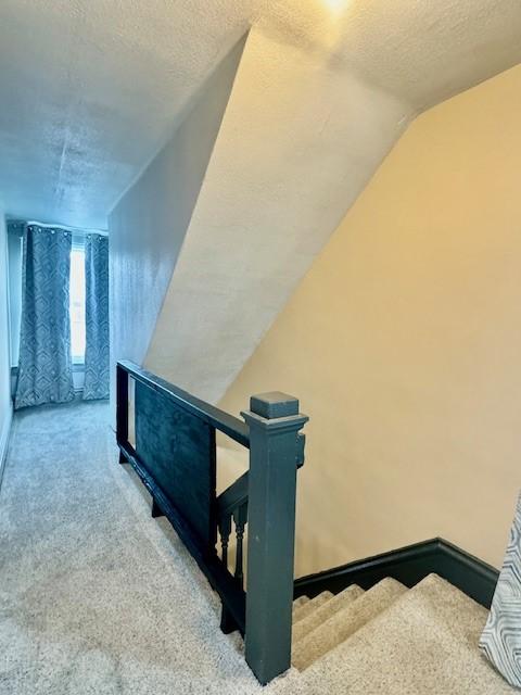 staircase with a textured ceiling, carpet floors, and vaulted ceiling