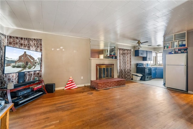 living room with ceiling fan, light wood-type flooring, sink, and a brick fireplace