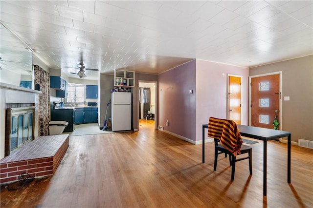 interior space with light wood-type flooring, a brick fireplace, and ceiling fan