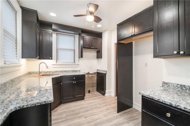 kitchen with light wood-type flooring, light stone counters, ceiling fan, and sink