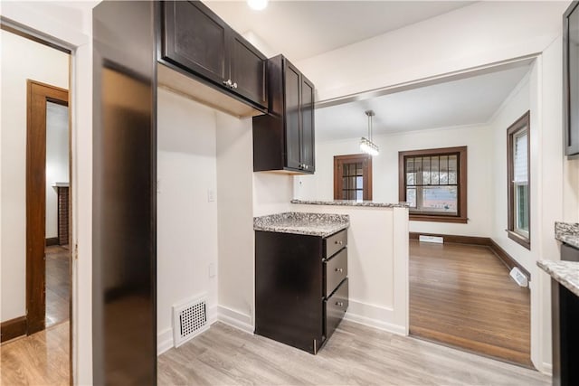 kitchen with pendant lighting, dark brown cabinets, light stone countertops, and light hardwood / wood-style flooring