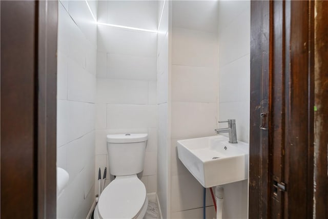 bathroom with toilet, sink, and tile walls