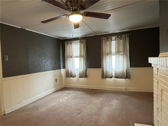 carpeted empty room featuring a brick fireplace and ceiling fan