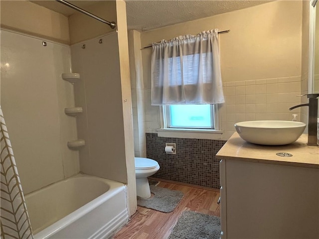 full bathroom featuring a textured ceiling, toilet, vanity, tile walls, and hardwood / wood-style flooring