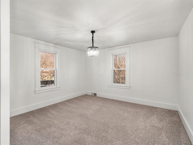 carpeted spare room with an inviting chandelier