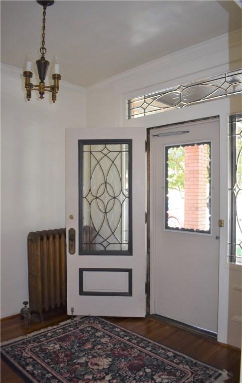 entrance foyer with radiator heating unit, dark wood-type flooring, an inviting chandelier, and ornamental molding