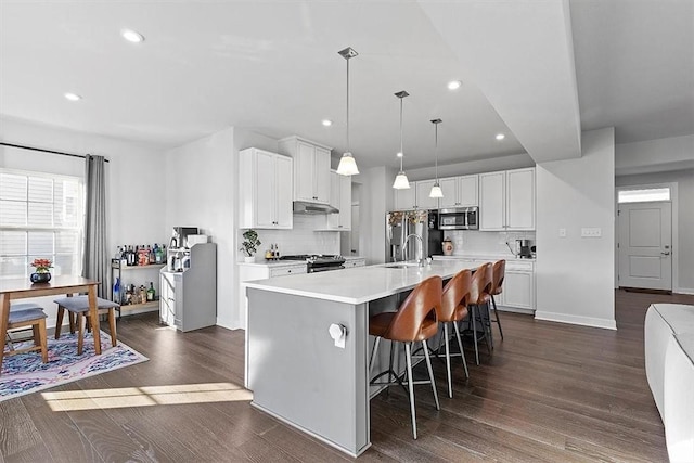 kitchen with pendant lighting, stainless steel appliances, white cabinetry, and an island with sink