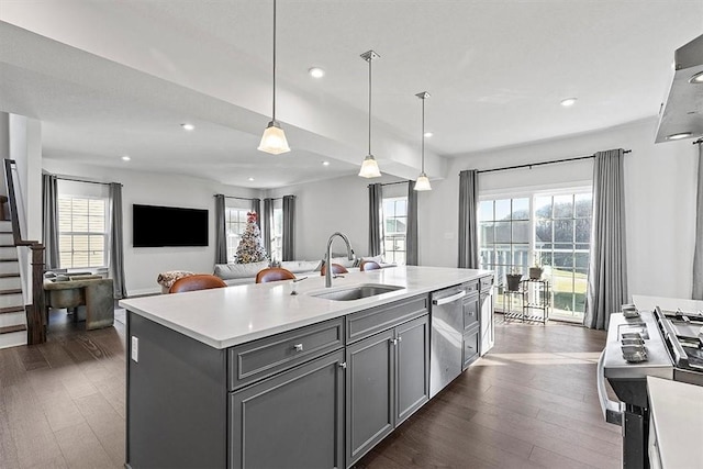 kitchen with gray cabinetry, stainless steel appliances, sink, decorative light fixtures, and a center island with sink