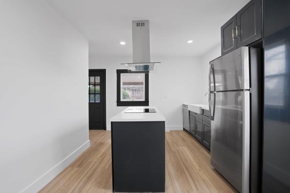 kitchen featuring black electric stovetop, light hardwood / wood-style flooring, a kitchen island, island exhaust hood, and stainless steel refrigerator